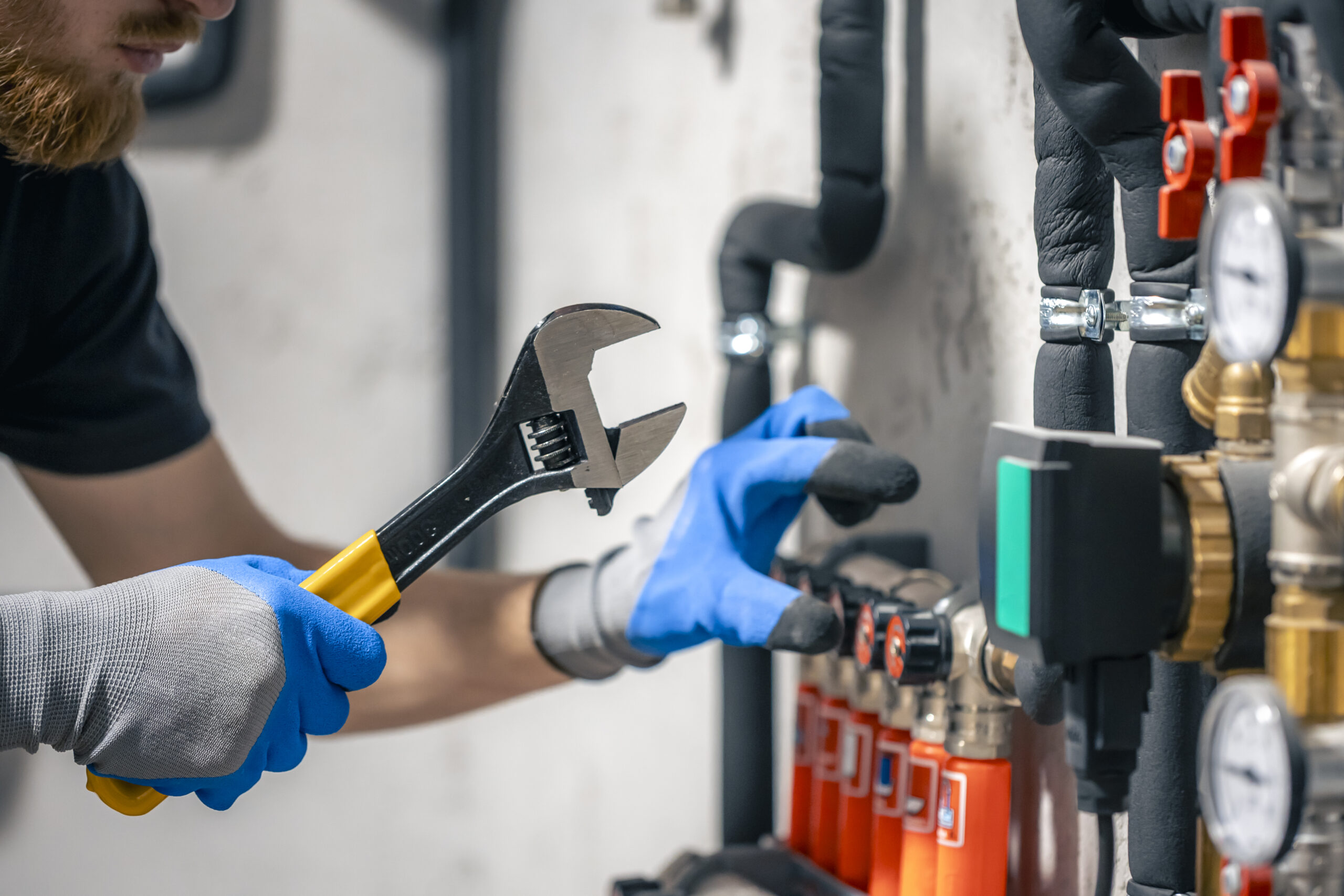 A man installs a heating system in a house and checks the pipes with a wrench. Adjusting heating valves in a residential building. A plumbing and heating technician works.